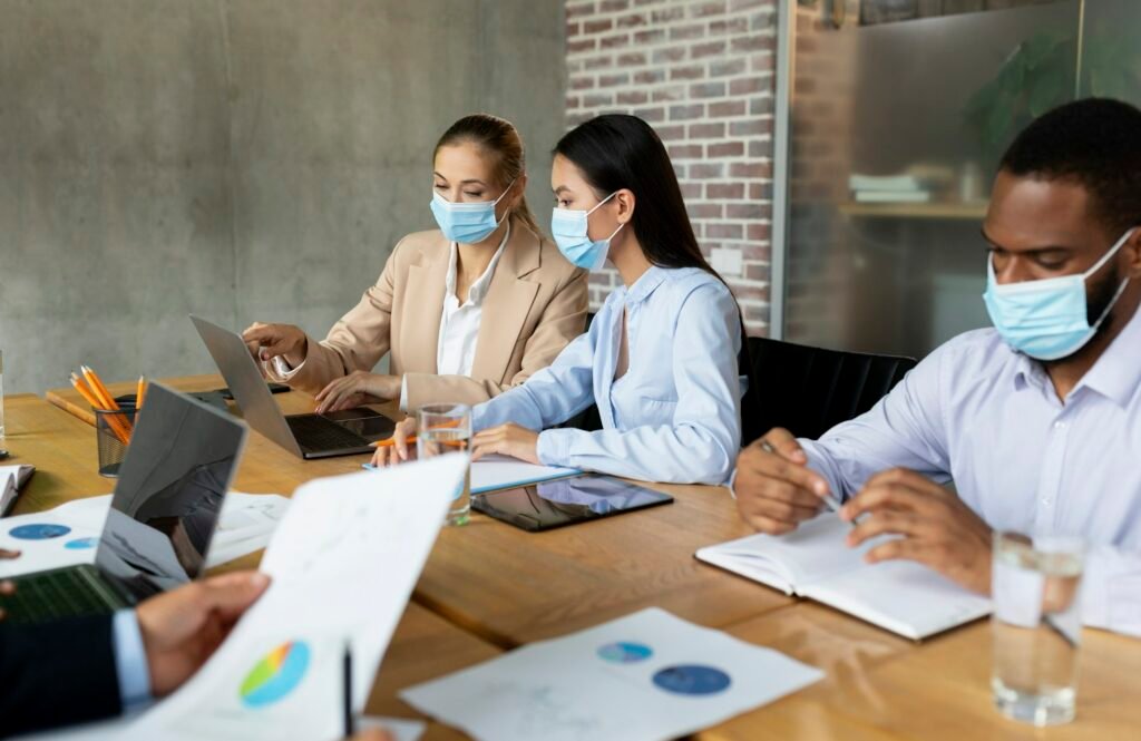 Business People In Protective Face Masks Having Corporate Meeting In Office